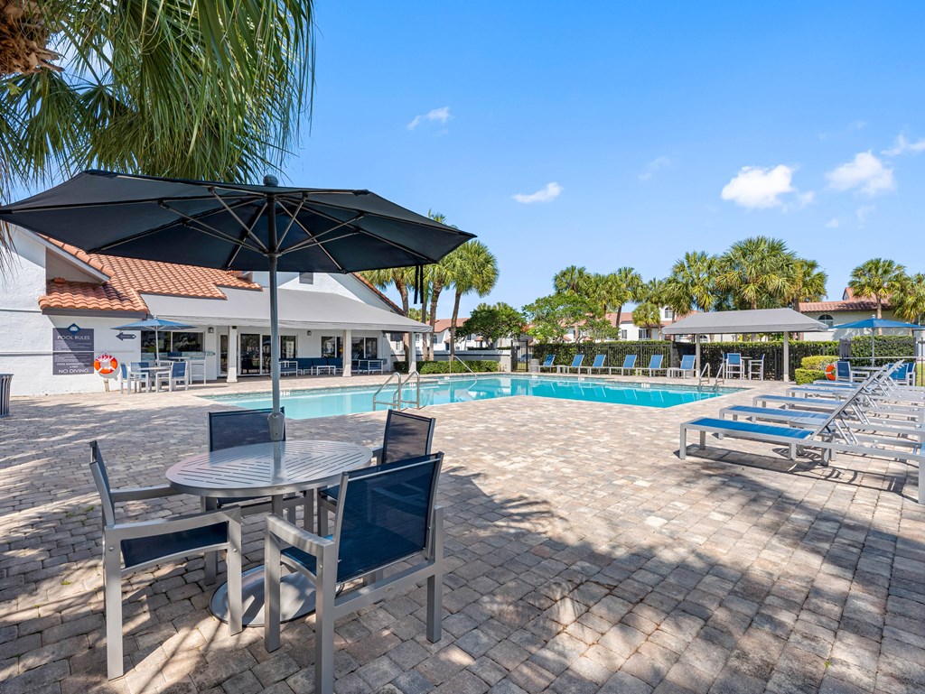A poolside area with a table and chairs and a black umbrella.